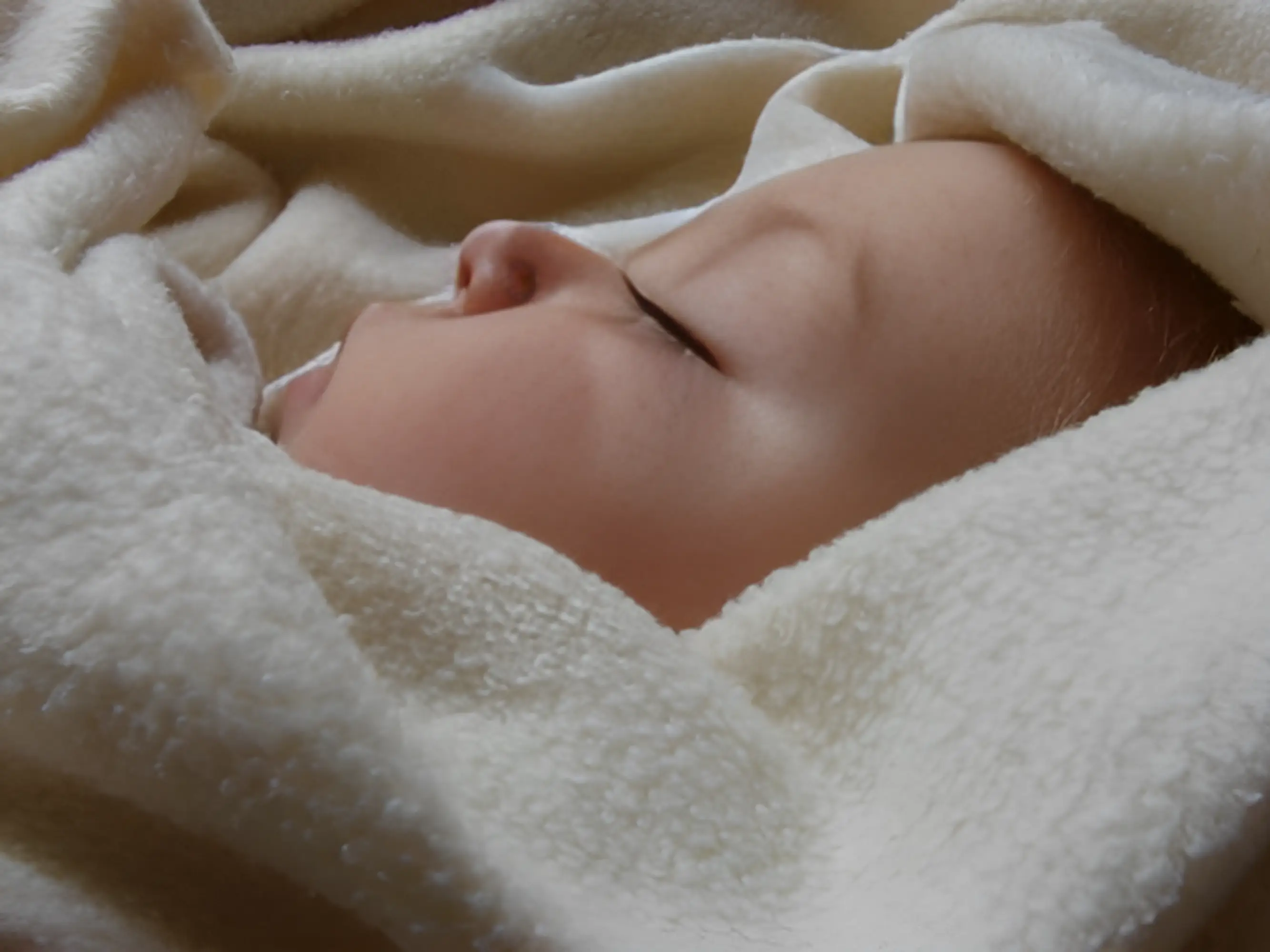 A sleeping baby wrapped in a soft, white blanket.