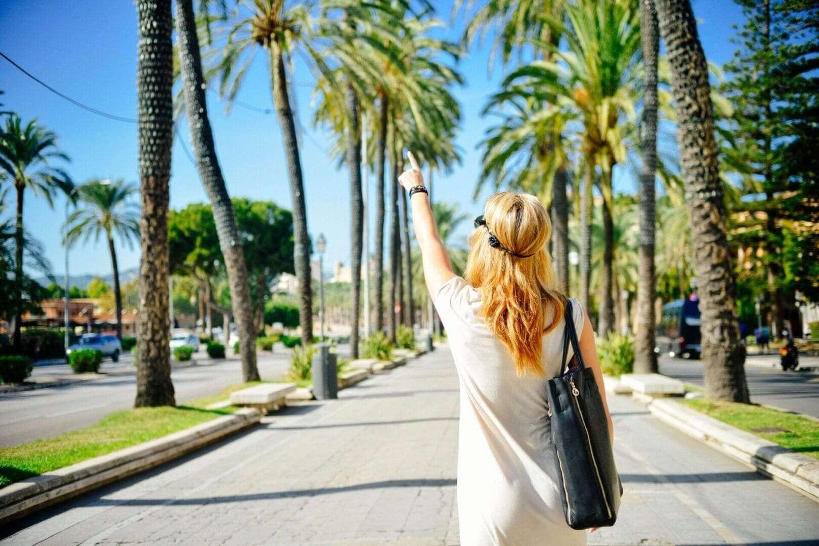 Woman pointing toward palm-lined sunny promenade