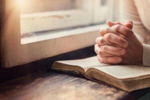 Hands folded in prayer over open Bible