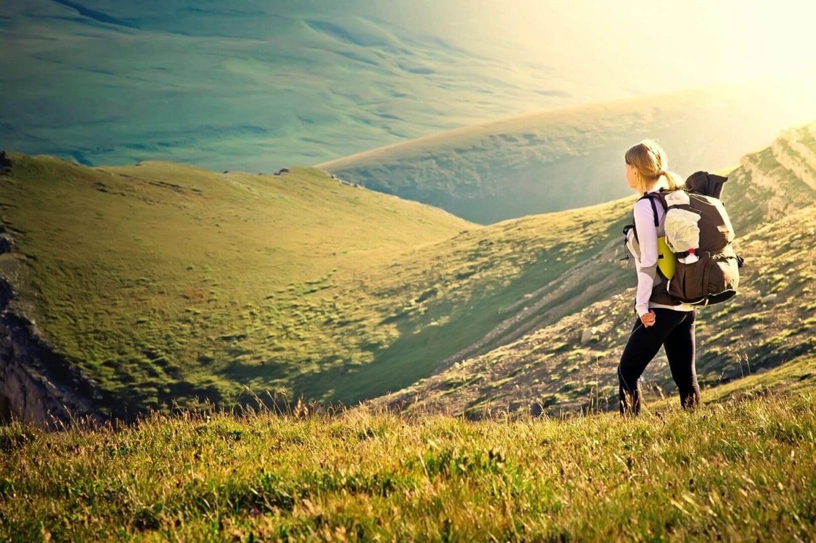 Backpacker overlooking sunlit rolling green hills